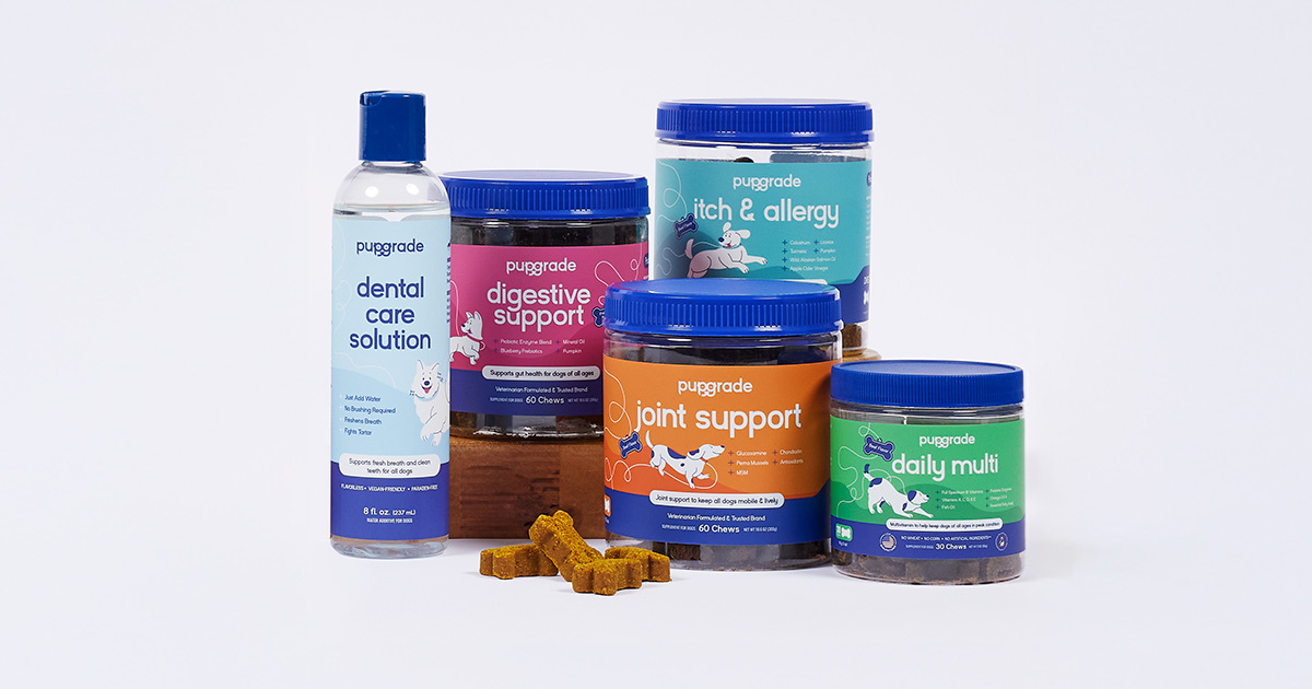 A variety of PupGrade dog supplements arranged on a light background. From left to right: a bottle of dental care solution, a container of digestive support chews, a container of itch & allergy chews, a container of joint support chews, and a container of daily multi vitamin chews. Several bone-shaped chews are scattered in front of the containers.
