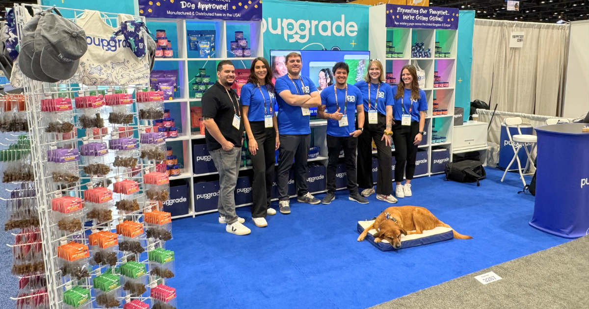 A group of six PupGrade team members stand in front a booth with pet supplies and a dog lying on a bed in the foreground.