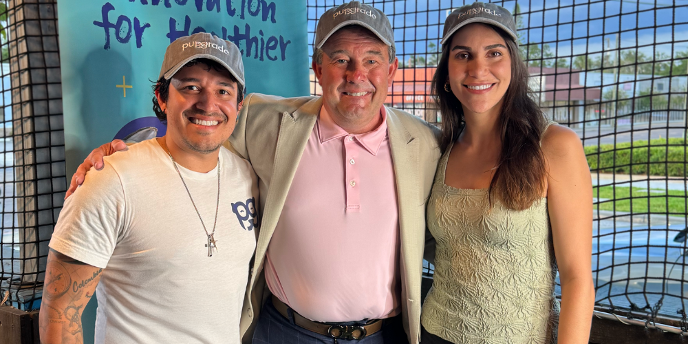 Three smiling individuals wearing Pupgrade hats posing in front of a Pupgrade backdrop