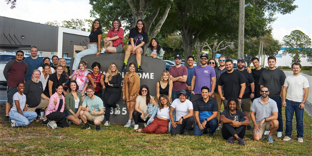 A large group of Wholesome Goods team members smiling and posing together outside the company headquarters, reflecting a warm, inclusive, and diverse workplace culture.