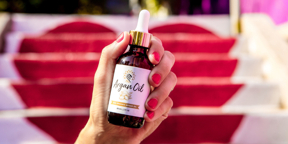 Hand holding Wholesome Goods Argan Cosmetics 100% Organic Argan Oil, natural multitasker for skin, hair, and nails