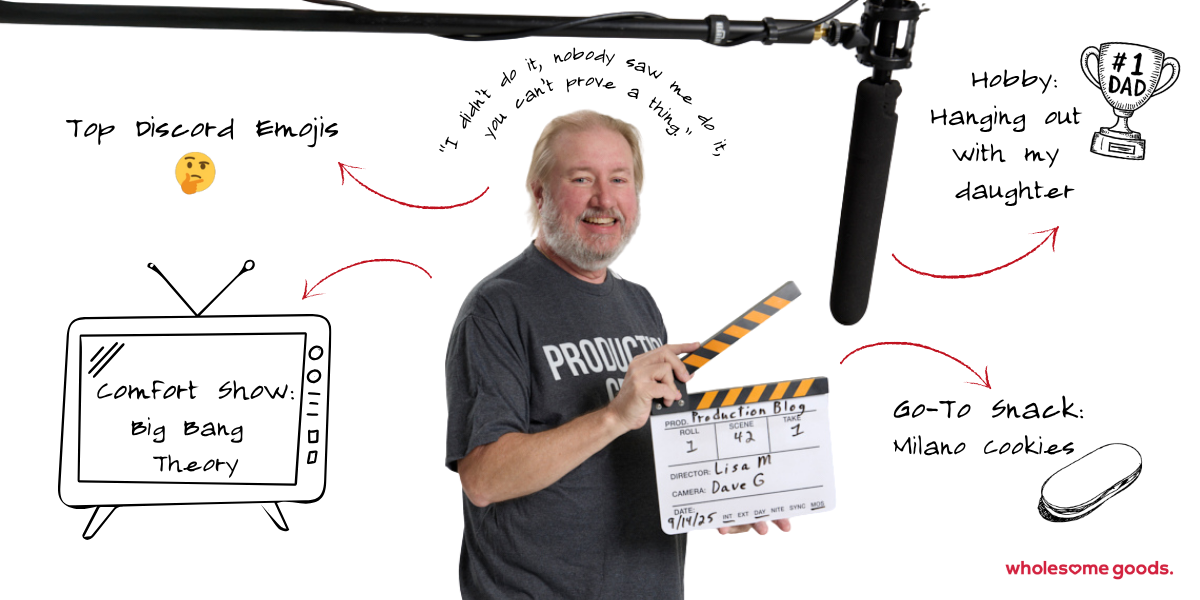 Wholesome Goods Production Manager Gerry holding a clapperboard under a boom mic on set, smiling mid-shoot.