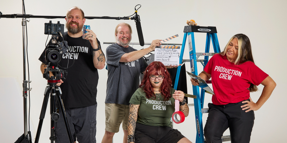 Wholesome Goods Production Team on set posing with gear—camera, clapperboard, ladder, and tools—wearing “Production Crew” shirts.