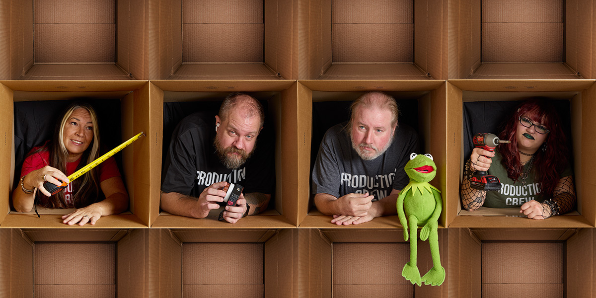 Wholesome Goods Production Team in studio setup, each member posing with tools of the trade inside cardboard boxes.