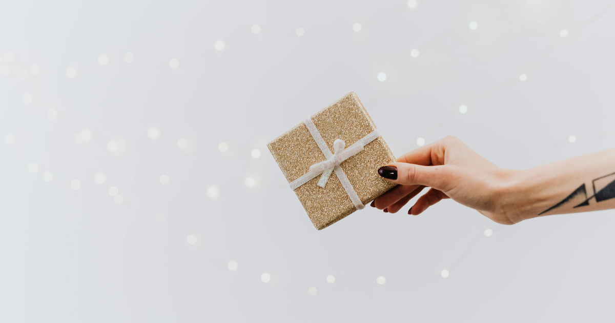 a hand holding a small gift wrapped in gold paper with a white bow