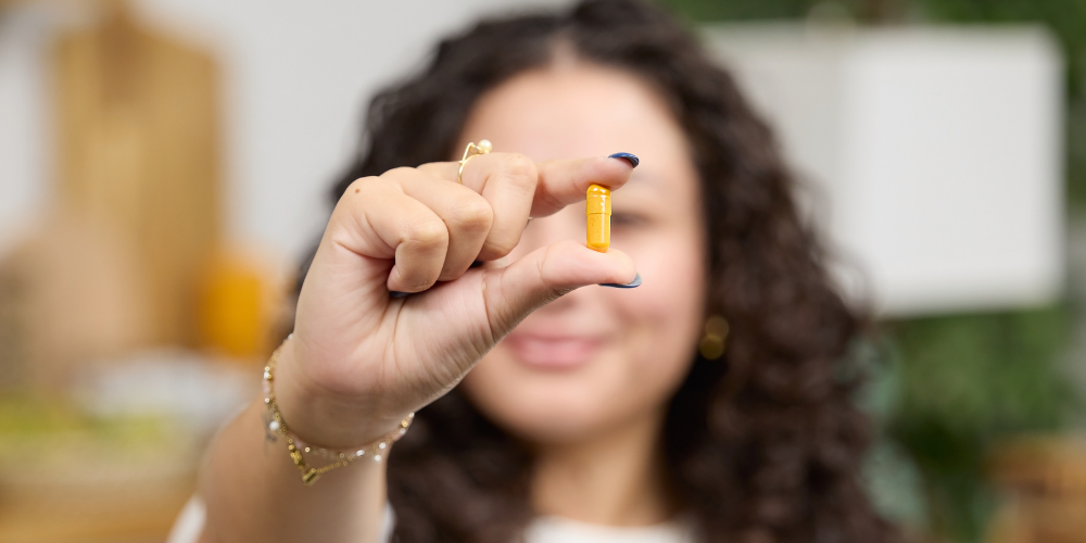 Young woman holding up a Pattern Wellness Turmeric capsule